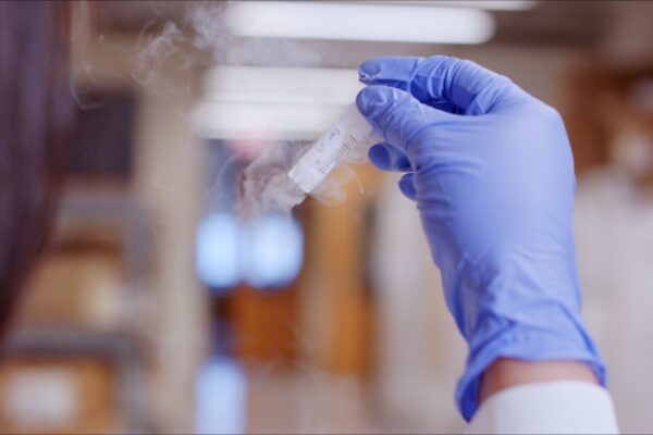 A close-up image of a biomedical researcher wearing rubber gloves and holding a vial containing samples