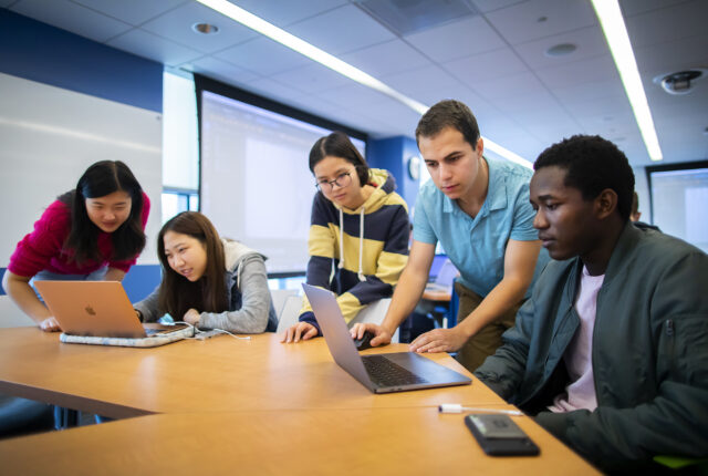 A small group of students sitting together around a table viewing material on laptops