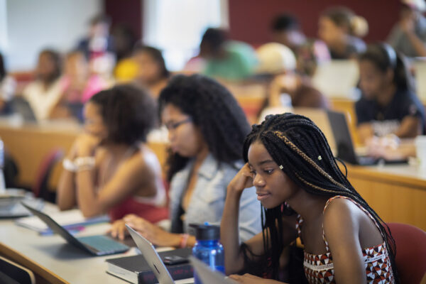 Students seated in classroom engaged in a lecture and viewing laptops