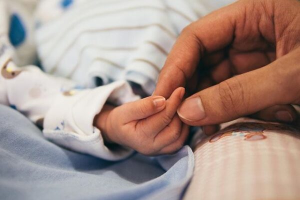 An adult hand holding a newborn baby's hand